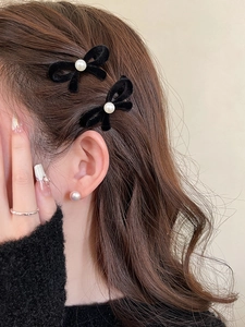 Detail of a black velvet bow hair clip with a pearl center on a woman's wavy brown hair