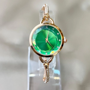 Elegant gold women's watch with green dial and rhinestone bracelet shown on stand