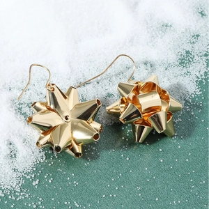 Detailed view of golden 3D gift bow earrings on decorative snow and green surface