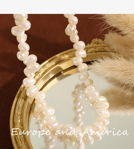 Detail view of baroque pearl necklace on a gold-framed mirror with feather decoration