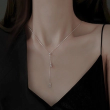 Dettaglio macro di una collana a Y argento con accenti di zircone su una modella