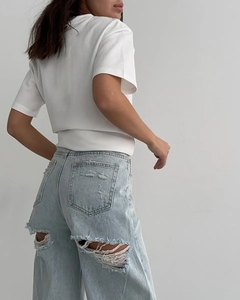 Détail d'un jean bleu clair usé avec des trous effilochés et une poche arrière