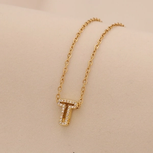 Macro shot of gold initial T pendant with sparkling crystals on minimalist chain