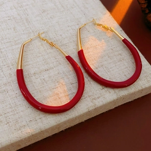 Detail of red enamel U-shaped hoop earrings with gold metal on textured beige fabric