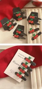 Detail view of sweet cherry hair clips with red resin fruit and green leaves on black base