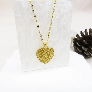 Detailed view of a gold heart pendant with a hammered texture on a marble display