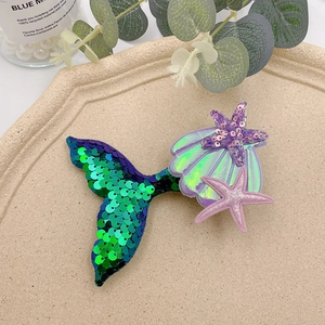 Detail of sequin mermaid tail hair clip with purple shell and starfish in a tray