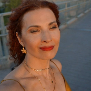 Detail of 18K gold starfish earrings and layered heart necklaces on a model at sunset