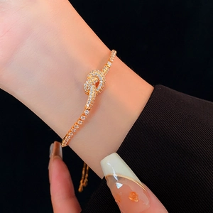 Detail of gold knot bracelet with micro-pave zircons worn on wrist over black background