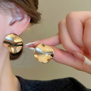 Detailed close-up of chunky gold irregular wave round stud earrings worn on the ear