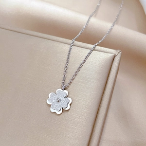 Detailed close-up of a silver four-leaf clover pendant on silk jewelry packaging