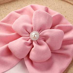 Close-up of pink baby turban hat with large fabric flower and pearl bead decorations