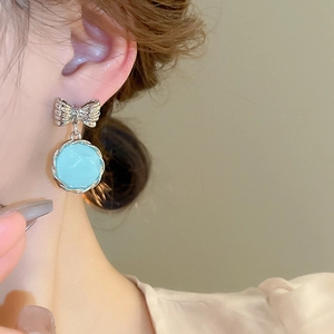 Close-up of bow-knot silver earrings with blue resin drop on model's ear