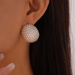 Close-up of a silver spherical earring with geometric texture worn by a model