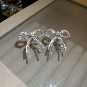 Close-up of silver bow earrings with sparkling diamonds and round pearls on a velvet tray