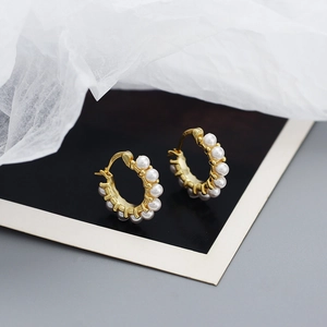 Detailed close-up of gold hoop earrings featuring delicate white pearls on gray backdrop