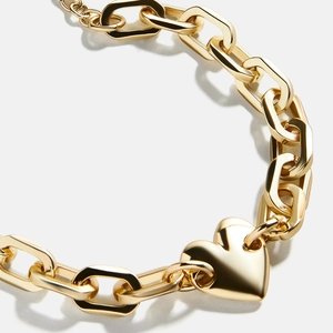 Macro detail of the golden heart pendant and thick curb chain texture on a white background
