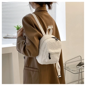 Detailansicht eines weißen Plüsch-Minirucksacks getragen über einem braunen Blazer