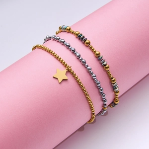 Detailed view of punk rock 18K gold and silver beaded bracelets with star charm on stand