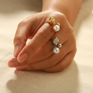 Lava textured 18K gold and silver rings with pearls worn on hands over linen background