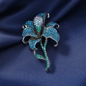 Elegant lily brooch with blue and green rhinestones on dark satin background
