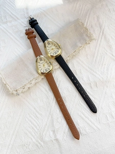 Detail view of gold snake-head watches with black and brown leather straps on beige fabric