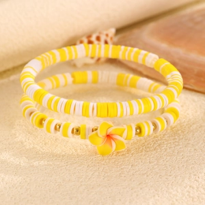 Dettaglio di braccialetti in perline Heishi gialle e bianche con fiori e tocchi oro