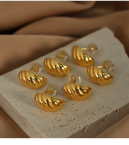 Detailed view of three pairs of gold ribbed C-shape earrings on a white stone base