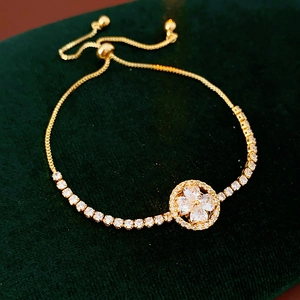Detail of adjustable gold-plated clover bracelet with zircon stones on green velvet