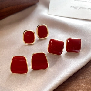 Detailed view of burgundy geometric enamel stud earrings on champagne silk fabric