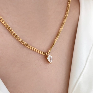 Detail of gold double-layered necklace with pear-cut zircon pendant on cuban chain