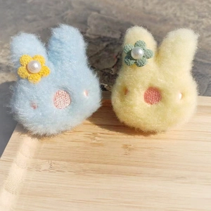 Plüsch-Hasen-Broschen in Blau und Gelb mit Perlen auf Holztablett im Sonnenlicht