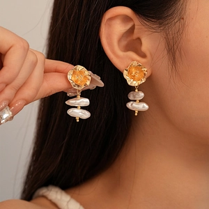 Detail of golden flower stud earrings with elegant baroque pearls worn on model ear