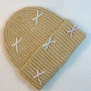 Detail view of khaki knit beanie featuring five colorful ribbon bows on a ribbed texture