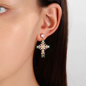 Cross earrings in gold plated brass with green zircon and white pearl worn by a model
