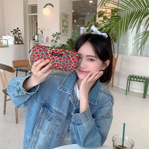 Floral corduroy stationery bag with logo patch held by a model in a cafe setting