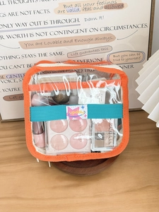 Close-up of square PVC makeup bag with orange trim and cosmetics shown on wooden table