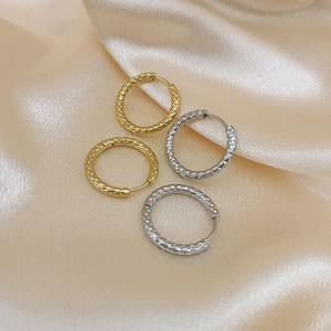 Detail of gold and silver titanium steel hoop earrings with textured finish on silk