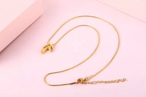 Close-up of golden V-shape pendant necklace with snake bone chain on pink background