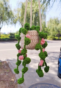 Detail of hand-crocheted hanging plant with pink flowers and green vines on beige pot