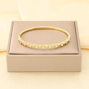 Dettaglio di bracciale rigido dorato in acciaio con cuori e cristalli scintillanti