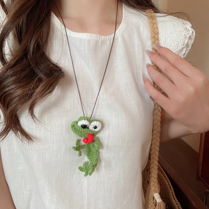 Close-up of a handmade crochet green frog pendant on a brown cord necklace