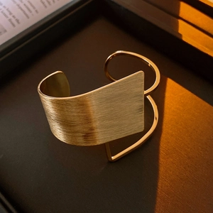 Macro detail of gold brushed metal cuff bracelet with geometric wire design on dark surface