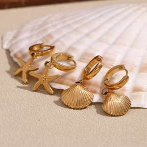Detail of 18K gold-plated starfish and seashell dangle earrings on white shell background