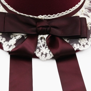 Detail of wine red wool cloche hat featuring satin bow and intricate white floral lace trim