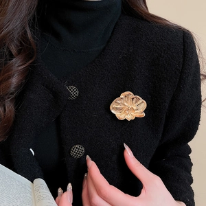 Detail of a golden orchid brooch featuring brushed metal texture on a black tweed blazer