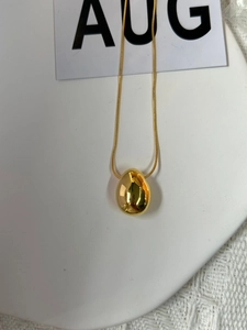 Macro detail of a minimalist gold teardrop pendant on a fine snake chain necklace