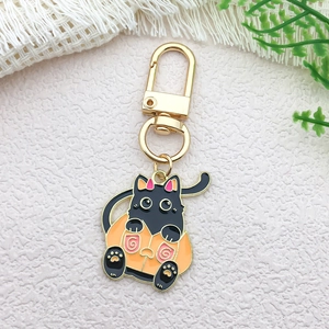 Detail of metal keychain featuring black cat in orange pumpkin costume on beige background