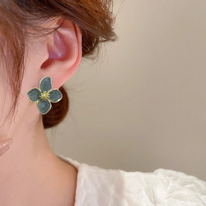 Close-up of elegant dark blue enamel flower earring with gold trim worn by a model