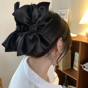 Detail of oversized black satin bow hair clip with layered fabric on model's hair
